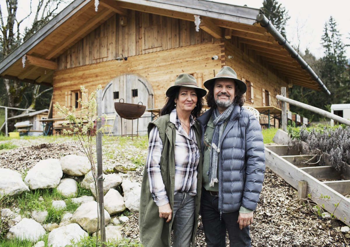 Frau  und Mann mit Hüten stehen vor Haus im Garten