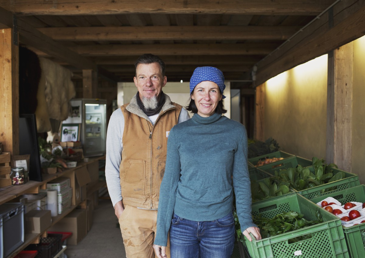 Mann und Frau stehen in ihrem Hofladen neben Gemüsekisten